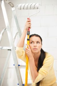 DIY or Professional Painters? Frustrated woman leans on ladder with paint roller