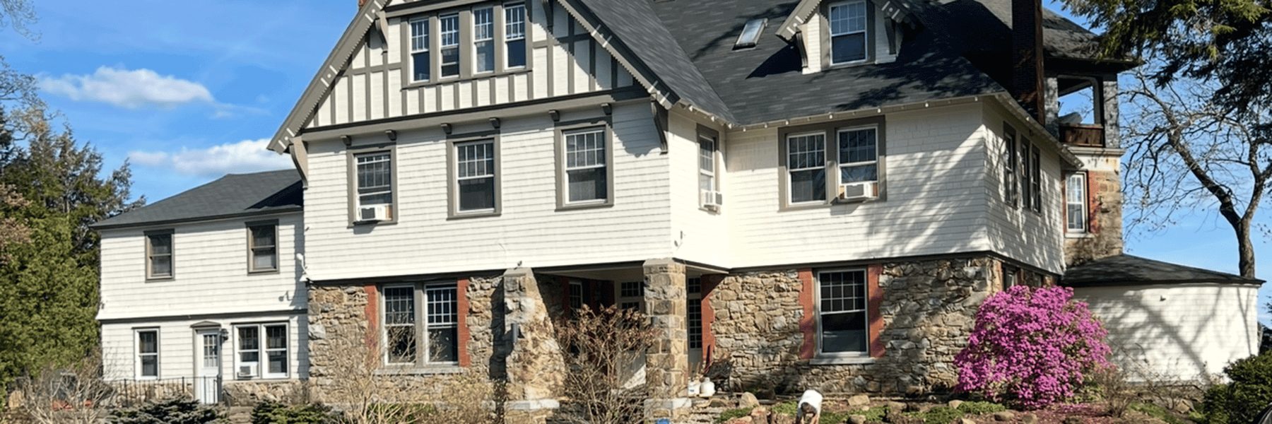 Commercial exterior painting project featuring a large historic stone and siding building with freshly painted white trim, dark roof, and updated windows for a professional finish