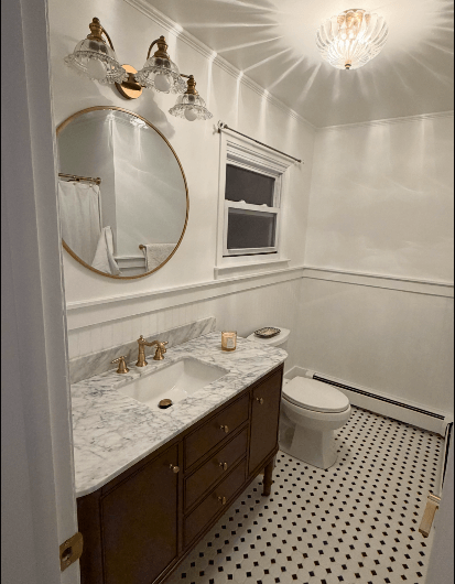 Updated bathroom remodel with marble vanity countertop, gold fixtures, round mirror, modern lighting, and black-and-white tile floor