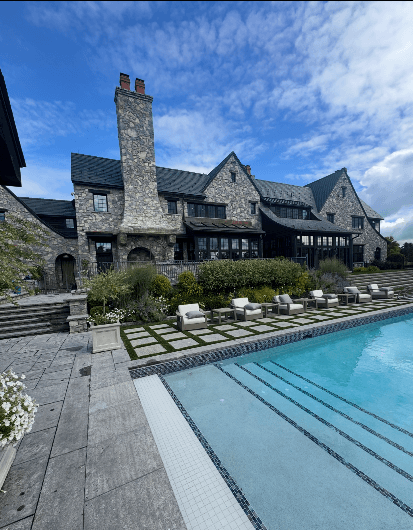 Large stone luxury home featuring freshly painted dark exterior trim and a backyard swimming pool, highlighting an exterior painting project in Greenfield Center, NY.